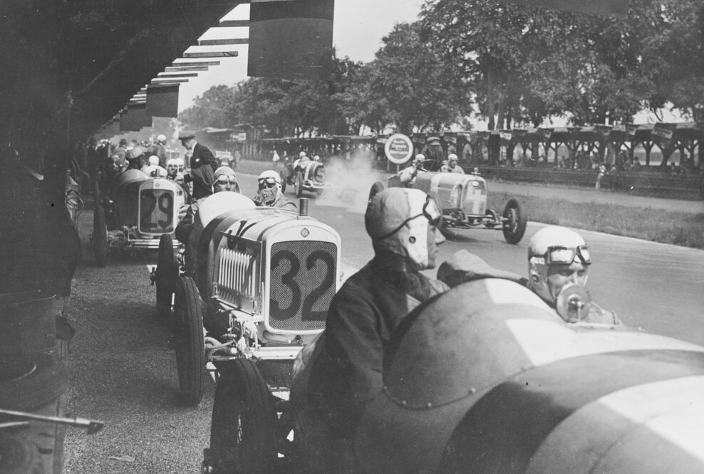 Großer Preis von Deutschland 1926 auf der Berliner AVUS: Die NSU Kompressor-Rennwagen NSU 6/60 PS stehen in den Boxen und warten auf die Freigabe des Starts. Im Wagen Nr. 32 der spätere Sieger in der 1,5-Liter-Klasse Georg Klöble mit Beifahrer Karl Gailing.