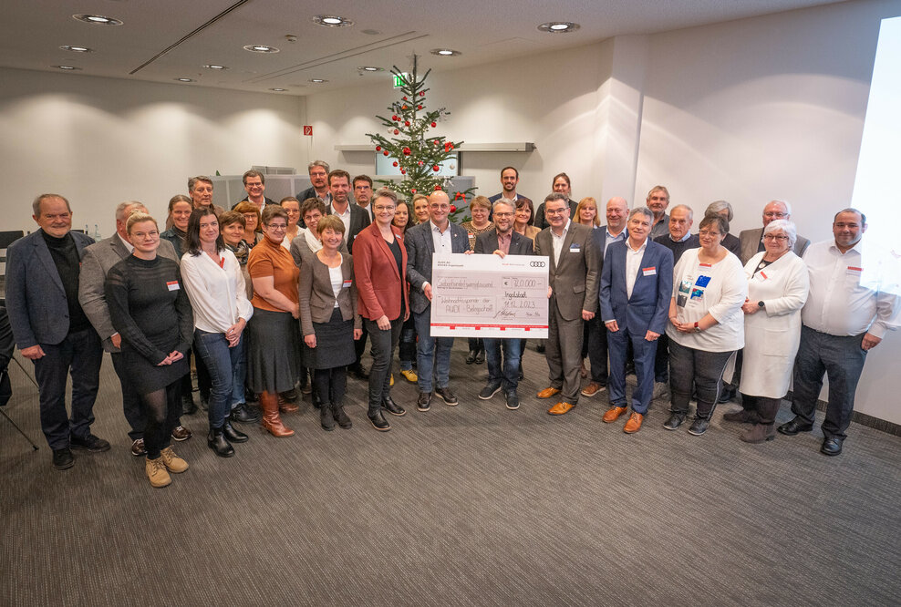 Der Betriebsrat übergibt den symbolischen Spendenscheck der diesjährigen Weihnachtsspende der Audi Belegschaft an die Vertreter_innen sozialer Organisationen aus der Region.