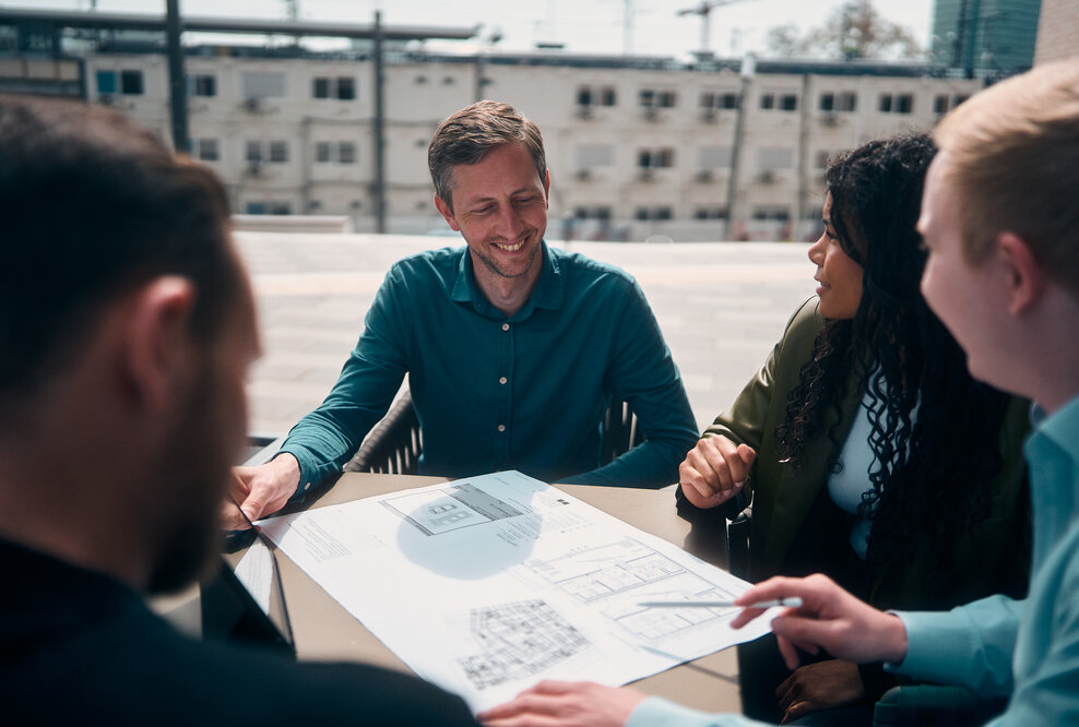 Team Planport bei der Arbeit an einem Tisch, auf dem ein Gebäudeplan liegt