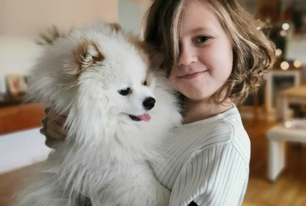 Ein Mädchen, dass einen weißen Hund auf dem Arm hält. 