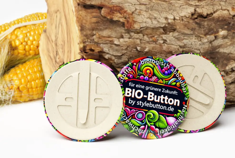 3 biologisch abbaubare Buttons von stylebutton.de, im Hintergrund sind ein Holzscheit und Maiskolben zu sehen
