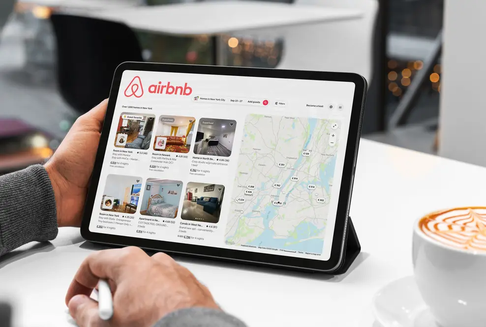 Mann sucht sich gerade auf einem Tablet auf Airbnb eine Unterkunft aus.