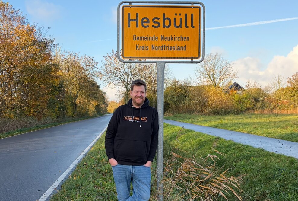 Martin Dellwing vor dem Ortseingangsschild von Hesbüll, Nordfriesland