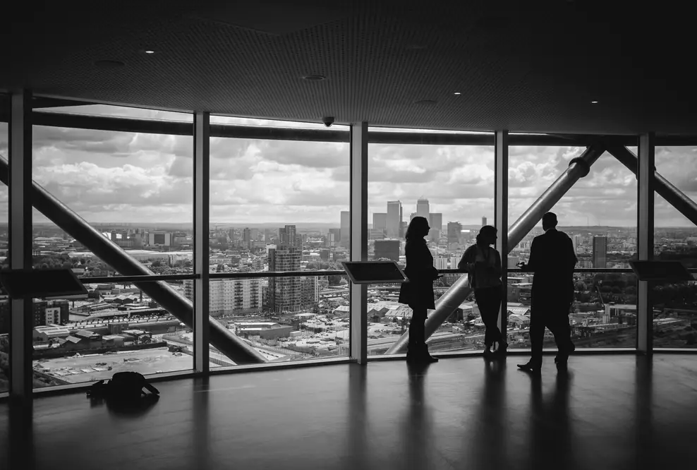 Drei Geschäftsleute stehen als Silhouetten vor einer Panoramafensterfront in einem modernen Hochhaus und besprechen ihre Marketingstrategie — symbolisch für strategische Unternehmensberatung im Bereich KMU Marketing.