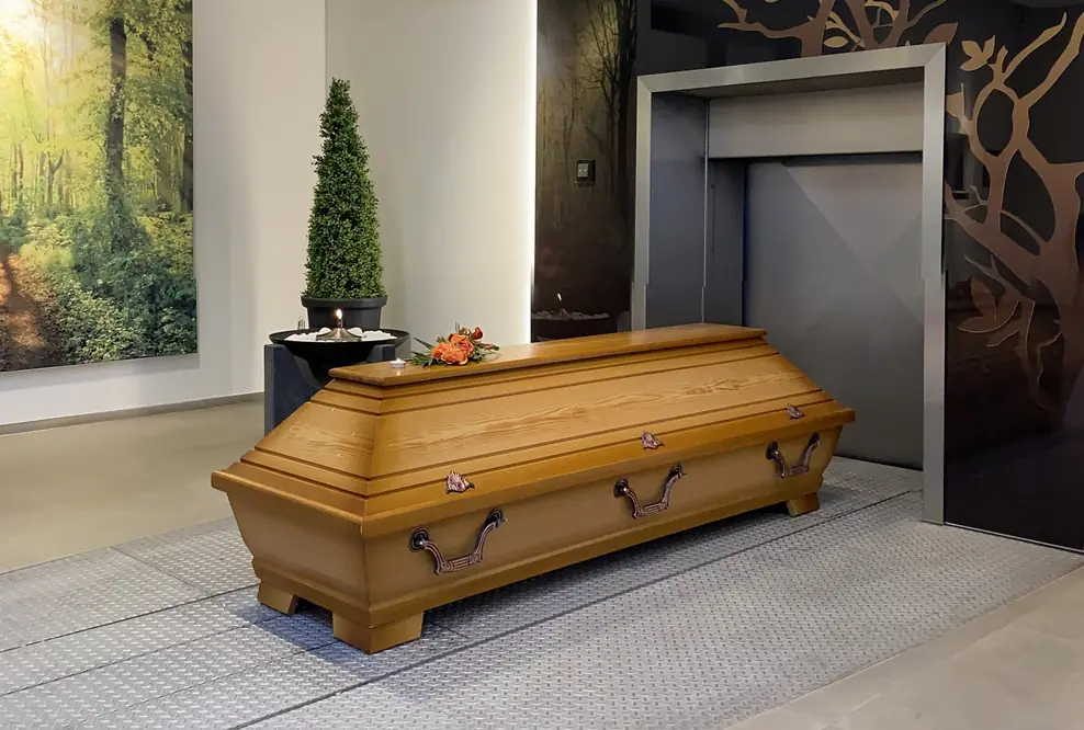 Ein Holzsarg mit Blumenschmuck und Teelicht steht vor einer Eiäscherungsanlage