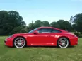 Porsche 911 Carrera S in Rot Seitenansicht steht auf grünem Gras, grüne Bäume im Hintergrund. Porsche 911 Carrera S symbolisiert Erfolg und Höchstleistungen wie die Highest-Quality-PR der DR. FALK KÖHLER PR © Foto: Dr. Falk Köhler / DR. FALK KÖHLER PR