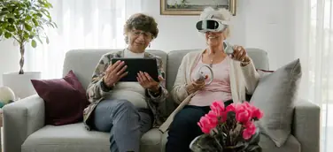 Seniorinnen mit VR-Brille und Tablet auf einem hellgrauen Sofa bei der Anwendung von teora mind