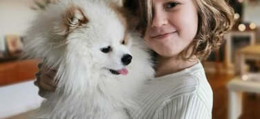 Ein Mädchen, dass einen weißen Hund auf dem Arm hält. 