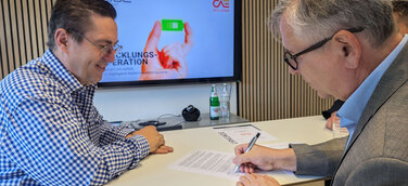 Jürgen Zinecker (AXSOL) und Dr. Hans-Peter Ebert (CAE) unterzeichnen die Entwicklungskooperation. (v. l. n. r.), Bildmaterial AXSOL GmbH 