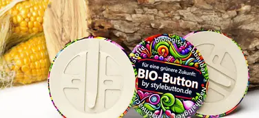 3 biologisch abbaubare Buttons von stylebutton.de, im Hintergrund sind ein Holzscheit und Maiskolben zu sehen