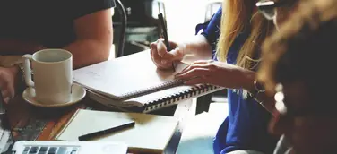 Gründerteam bei der gemeinsamen Arbeit am Tisch – Notizbücher, Laptop und Kaffeetasse im Einsatz, während sie einen Businessplan erstellen und Strategien für ihre Unternehmensgründung entwickeln..