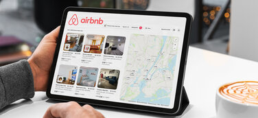 Mann sucht sich gerade auf einem Tablet auf Airbnb eine Unterkunft aus.