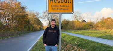 Martin Dellwing vor dem Ortseingangsschild von Hesbüll, Nordfriesland