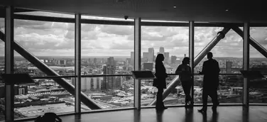 Drei Geschäftsleute stehen als Silhouetten vor einer Panoramafensterfront in einem modernen Hochhaus und besprechen ihre Marketingstrategie — symbolisch für strategische Unternehmensberatung im Bereich KMU Marketing.
