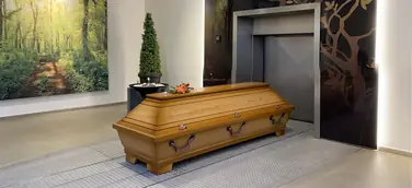 Ein Holzsarg mit Blumenschmuck und Teelicht steht vor einer Eiäscherungsanlage
