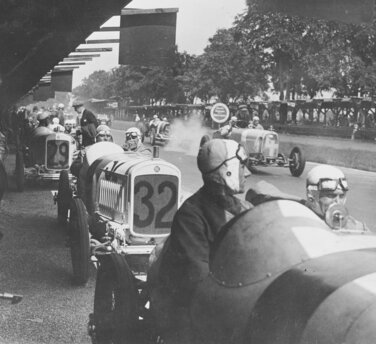 Großer Preis von Deutschland 1926 auf der Berliner AVUS: Die NSU Kompressor-Rennwagen NSU 6/60 PS stehen in den Boxen und warten auf die Freigabe des Starts. Im Wagen Nr. 32 der spätere Sieger in der 1,5-Liter-Klasse Georg Klöble mit Beifahrer Karl Gailing.