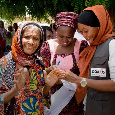 Zwei lachende nigerianische Frauen erhalten Hilfe von einer ZOA Mitarbeiterin