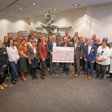 Der Betriebsrat übergibt den symbolischen Spendenscheck der diesjährigen Weihnachtsspende der Audi Belegschaft an die Vertreter_innen sozialer Organisationen aus der Region.