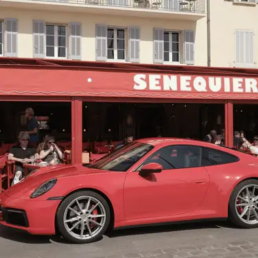 Porsche 911 Carrera S 992 in Rot Seitenansicht steht in Saint-Tropez vor dem roten Café SENEQUIER, im offenen Café sitzen Gäste