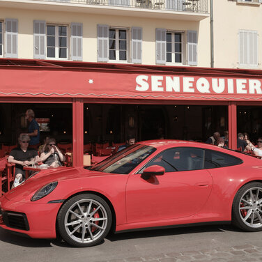 Porsche 911 Carrera S 992 in Rot Seitenansicht steht in Saint-Tropez vor dem roten Café SENEQUIER, im offenen Café sitzen Gäste