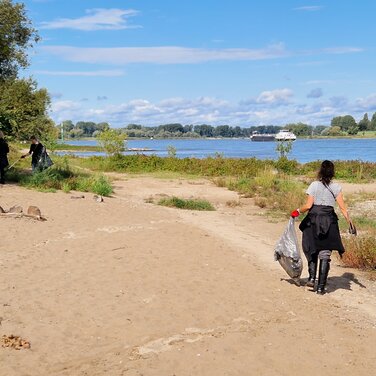 Eine Frau reinigt am Rhein den Müll