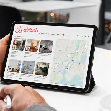 Mann sucht sich gerade auf einem Tablet auf Airbnb eine Unterkunft aus.