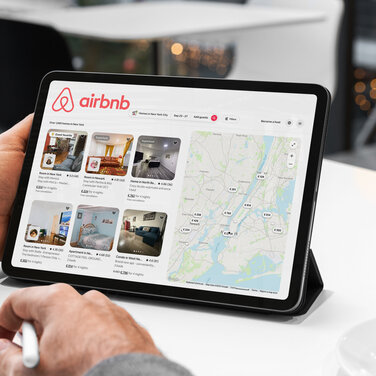 Mann sucht sich gerade auf einem Tablet auf Airbnb eine Unterkunft aus.