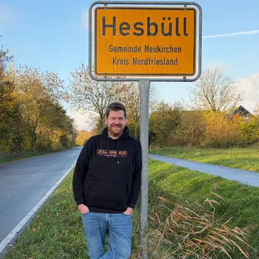 Martin Dellwing vor dem Ortseingangsschild von Hesbüll, Nordfriesland