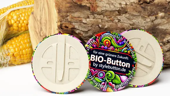 3 biologisch abbaubare Buttons von stylebutton.de, im Hintergrund sind ein Holzscheit und Maiskolben zu sehen