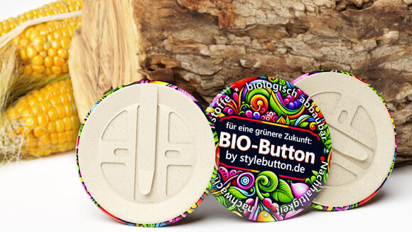3 biologisch abbaubare Buttons von stylebutton.de, im Hintergrund sind ein Holzscheit und Maiskolben zu sehen