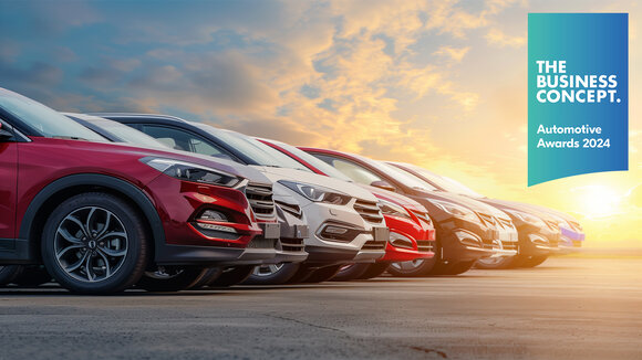 Text im Foto als Überschrift: The Business Concept. Automotive Awards 2024. Mehrere Autos in verschiedenen Farben wie Rot, Weiß, Grau stehen nebeneinander, Sicht jeweils von der Seite auf die Front jedes Autos bis zur Windschutzscheibe.