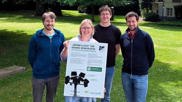 Das Team der SAUBER ENERGIE mit einem Hinweisschild, welches am Spielfeldrand über das Förderprojekt informiert