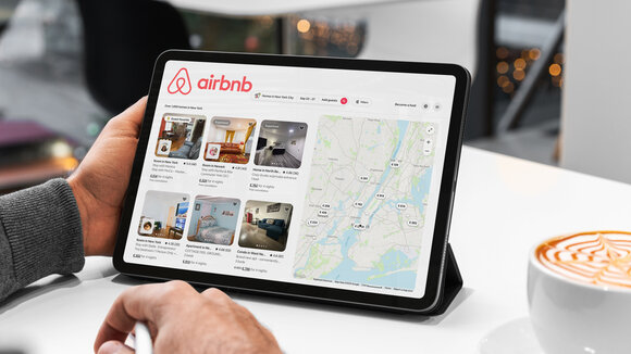 Mann sucht sich gerade auf einem Tablet auf Airbnb eine Unterkunft aus.