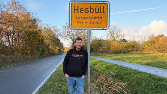 Martin Dellwing vor dem Ortseingangsschild von Hesbüll, Nordfriesland