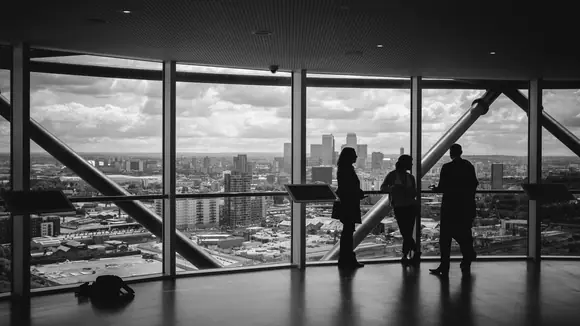 Drei Geschäftsleute stehen als Silhouetten vor einer Panoramafensterfront in einem modernen Hochhaus und besprechen ihre Marketingstrategie — symbolisch für strategische Unternehmensberatung im Bereich KMU Marketing.