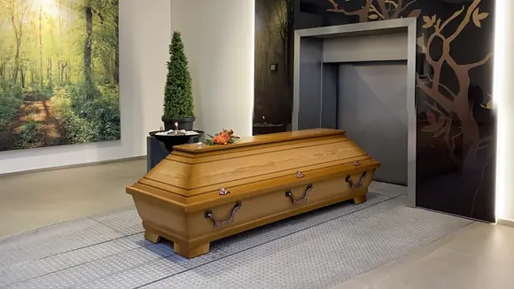 Ein Holzsarg mit Blumenschmuck und Teelicht steht vor einer Eiäscherungsanlage