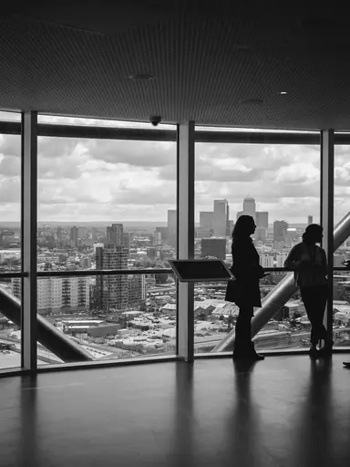 Drei Geschäftsleute stehen als Silhouetten vor einer Panoramafensterfront in einem modernen Hochhaus und besprechen ihre Marketingstrategie — symbolisch für strategische Unternehmensberatung im Bereich KMU Marketing.