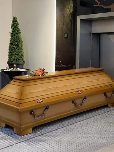 Ein Holzsarg mit Blumenschmuck und Teelicht steht vor einer Eiäscherungsanlage